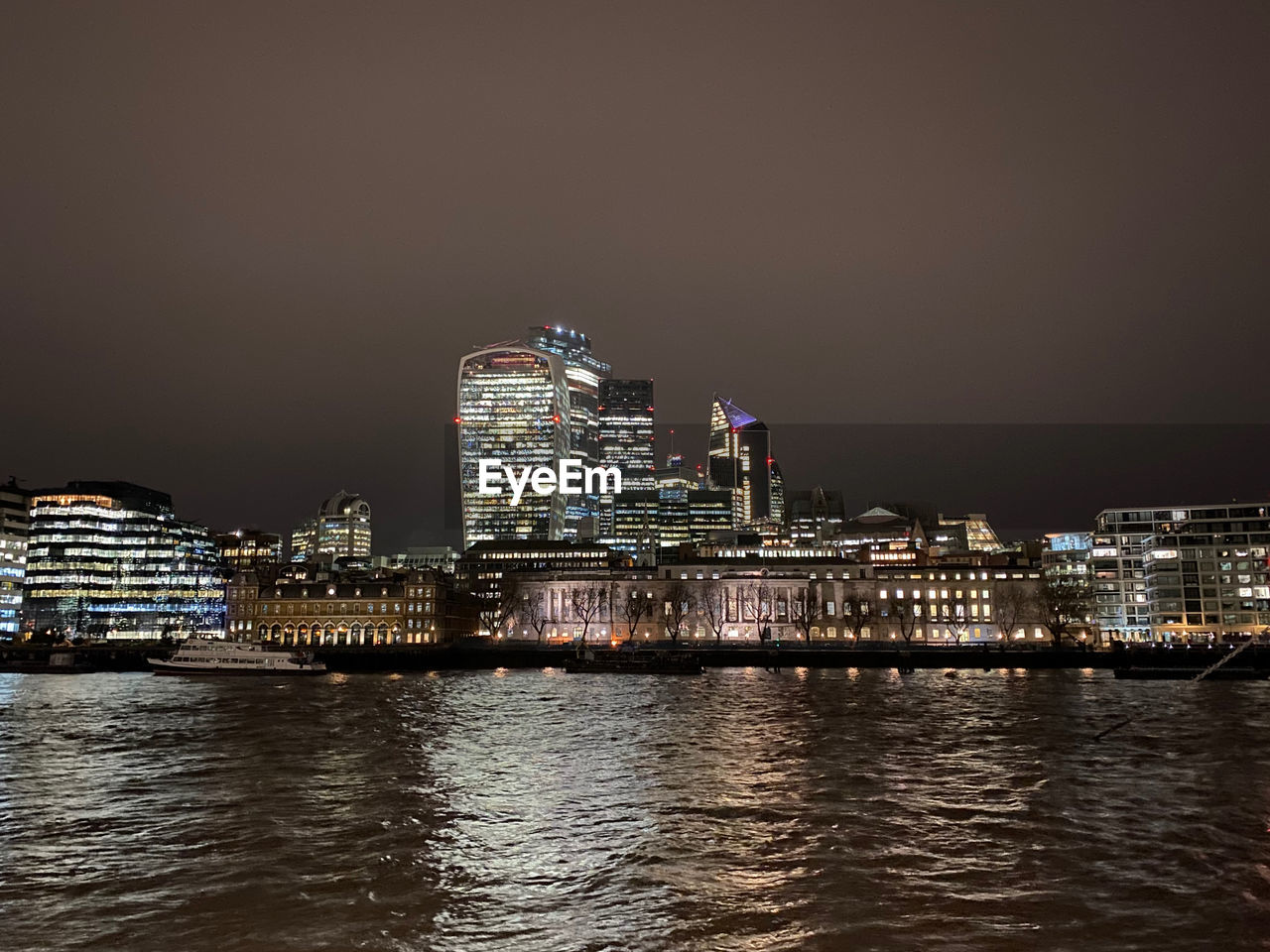 Illuminated buildings by thames river against sky at night in city of london