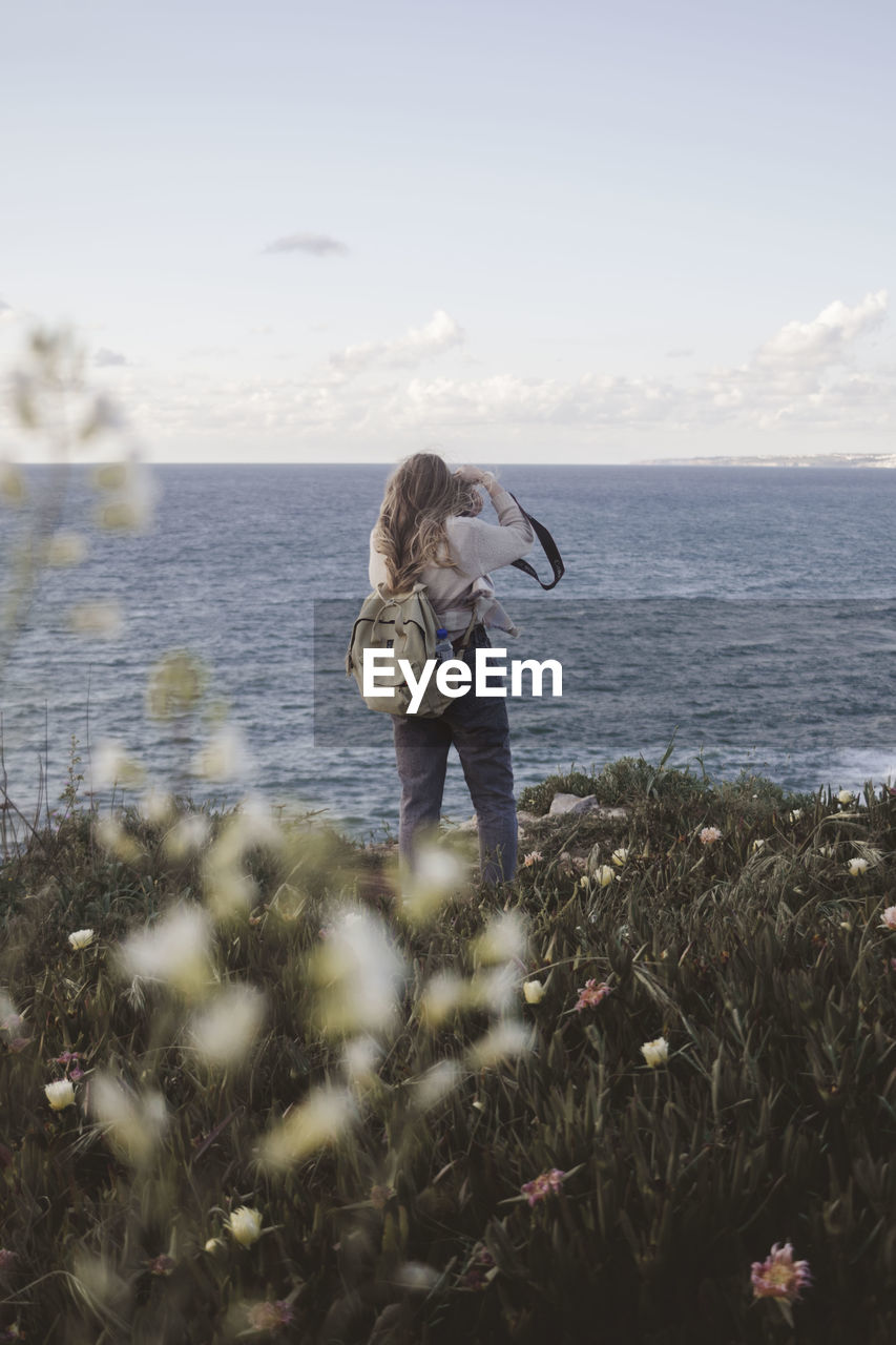 Woman with backpack standing by sea against sky