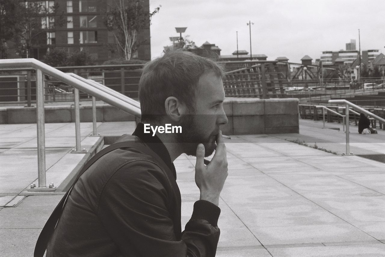 MAN SMOKING BY RAILING AGAINST SKY