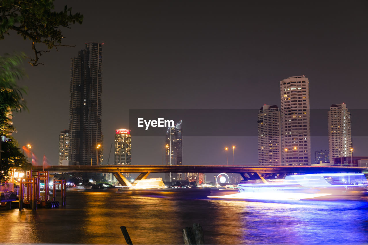 ILLUMINATED BUILDINGS BY RIVER AT NIGHT