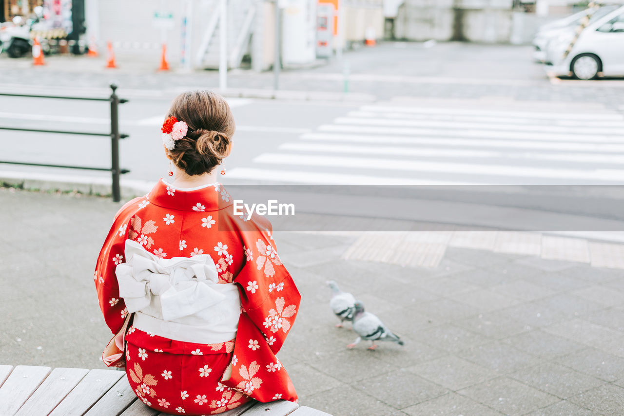 Rear view of woman in kimono sitting at city