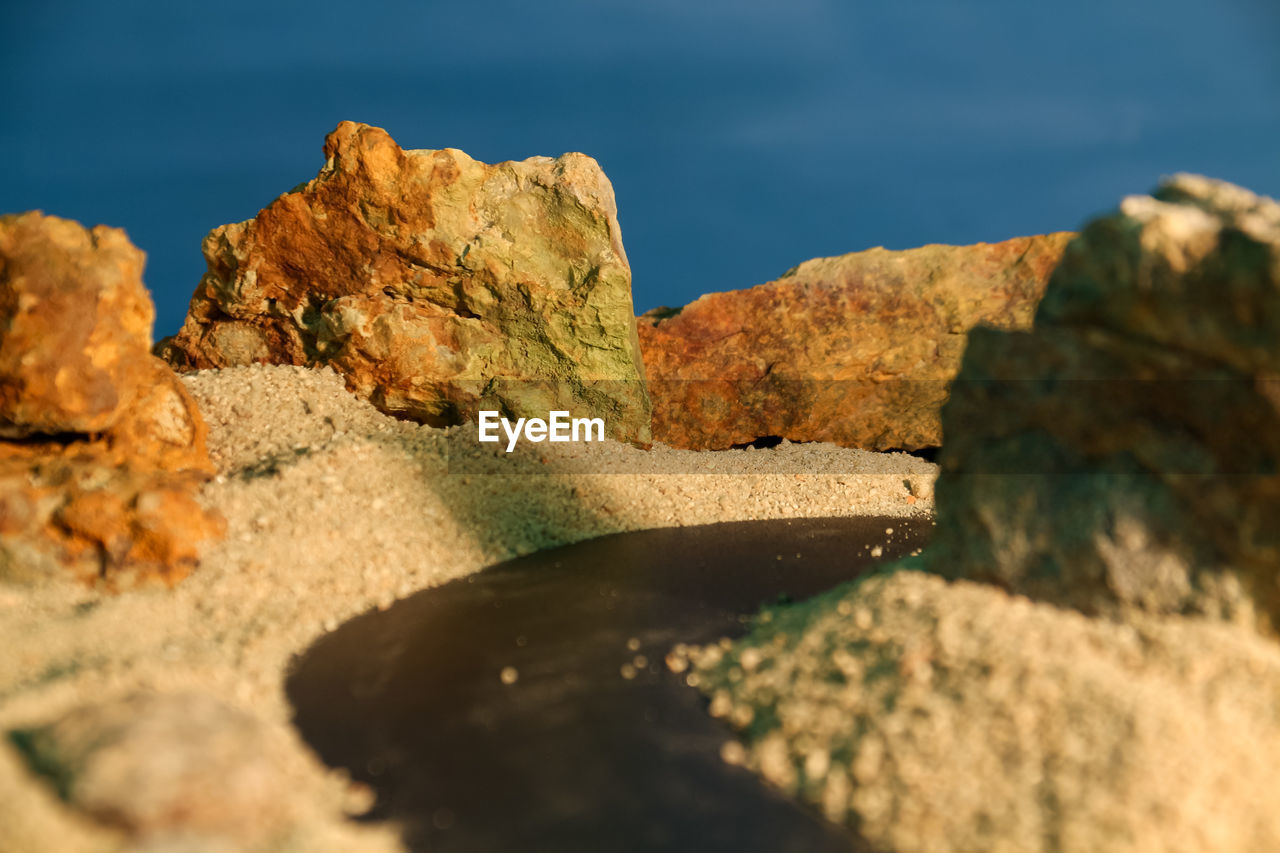 nature, rock, sea, water, land, sky, terrain, scenics - nature, coast, landscape, environment, beauty in nature, no people, rock formation, geology, reflection, travel destinations, travel, mountain, cliff, beach, outdoors, sunlight, tranquility, day, sand, blue, macro photography, ocean, non-urban scene, tranquil scene