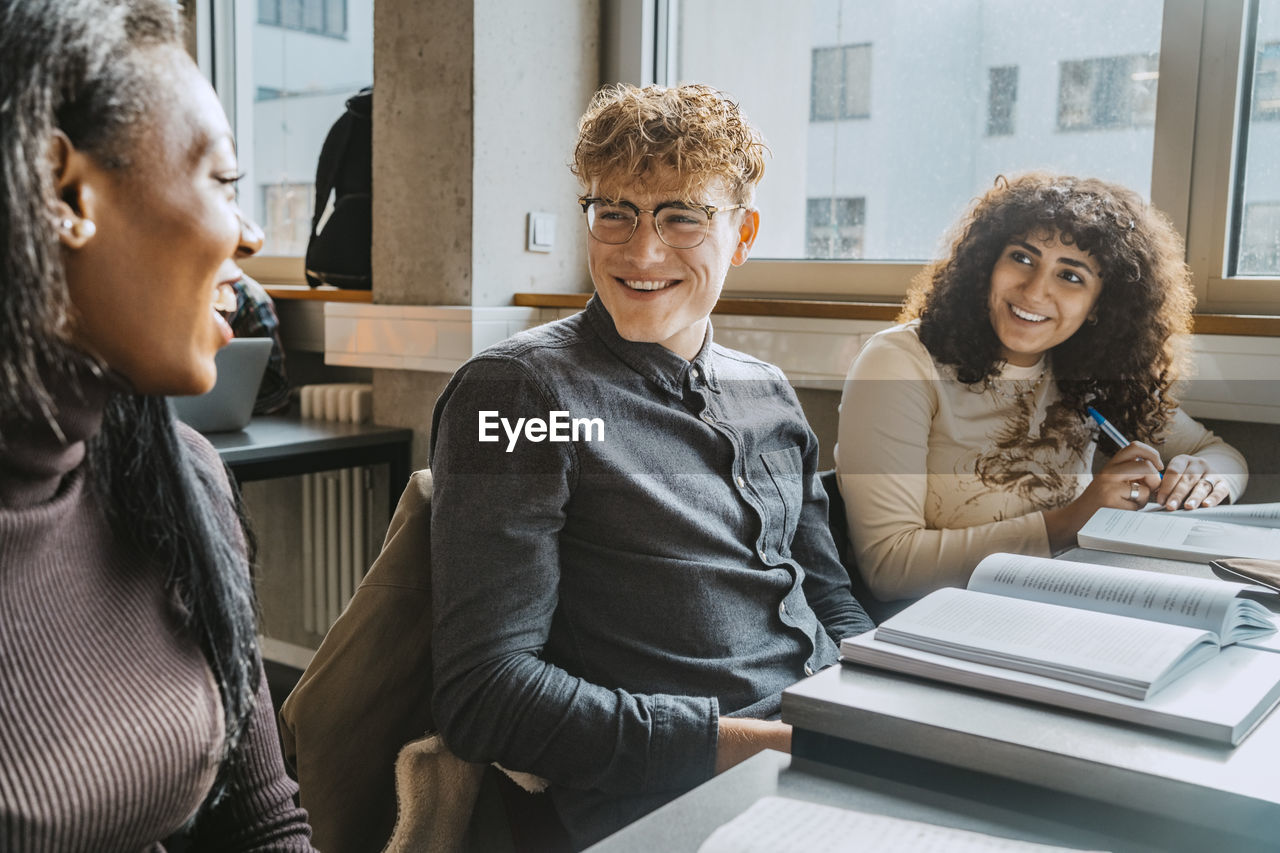 Cheerful multiracial friends talking while sitting in classroom in community college