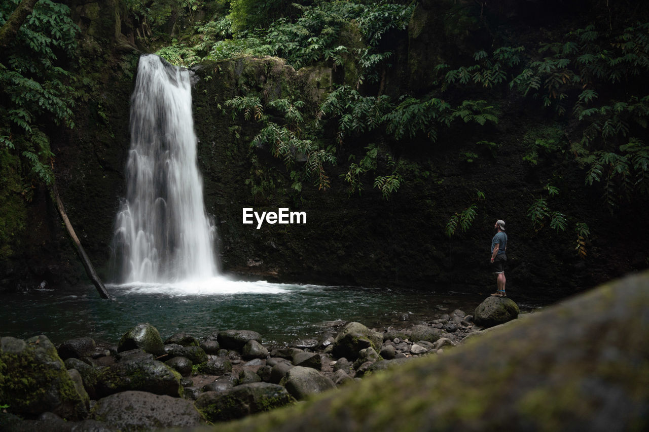 Scenic view of waterfall in forest with man watching 