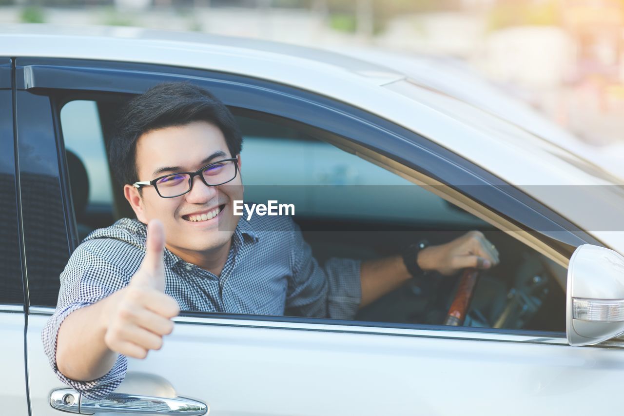 Portrait of smiling man gesturing thumbs up while sitting in car