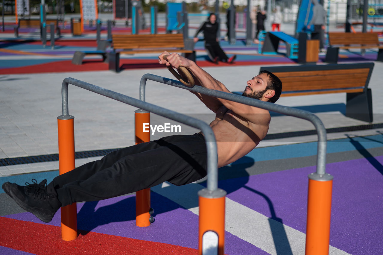 Shirtless man doing handstand on parallel bars at sports ground. 