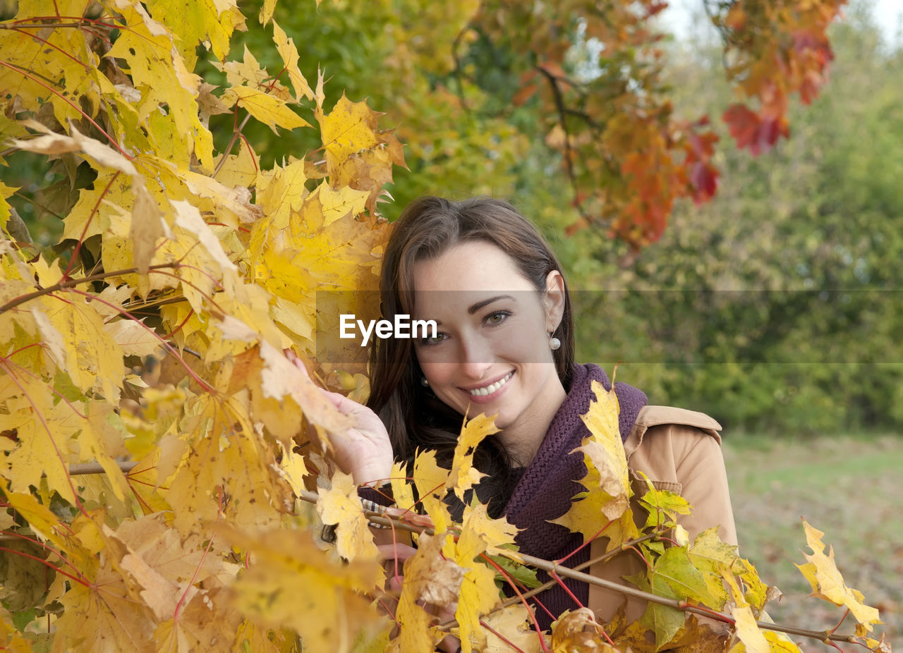 Portrait of woman wearing coat standing by trees in park during autumn