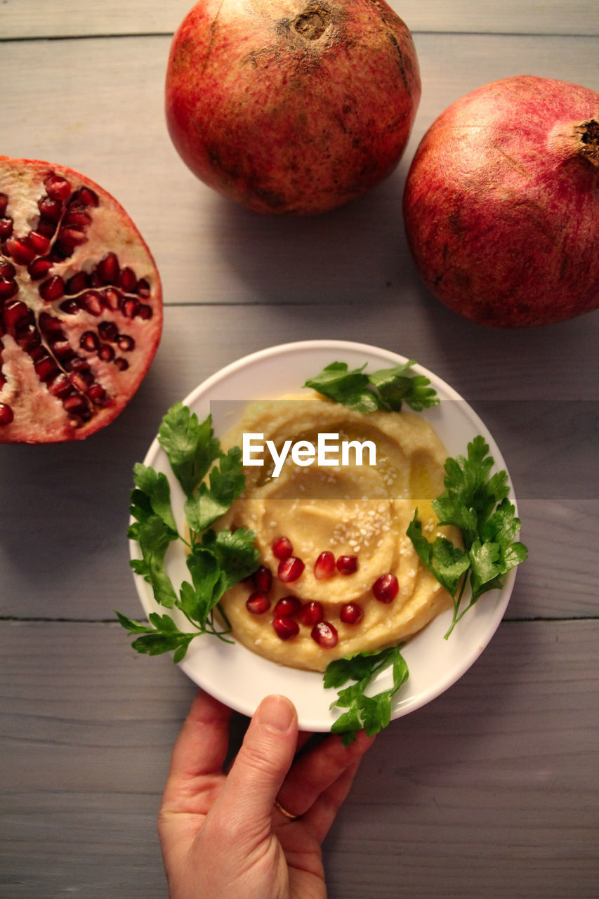 High angle view of hand holding hummus with pomegranate grains 
