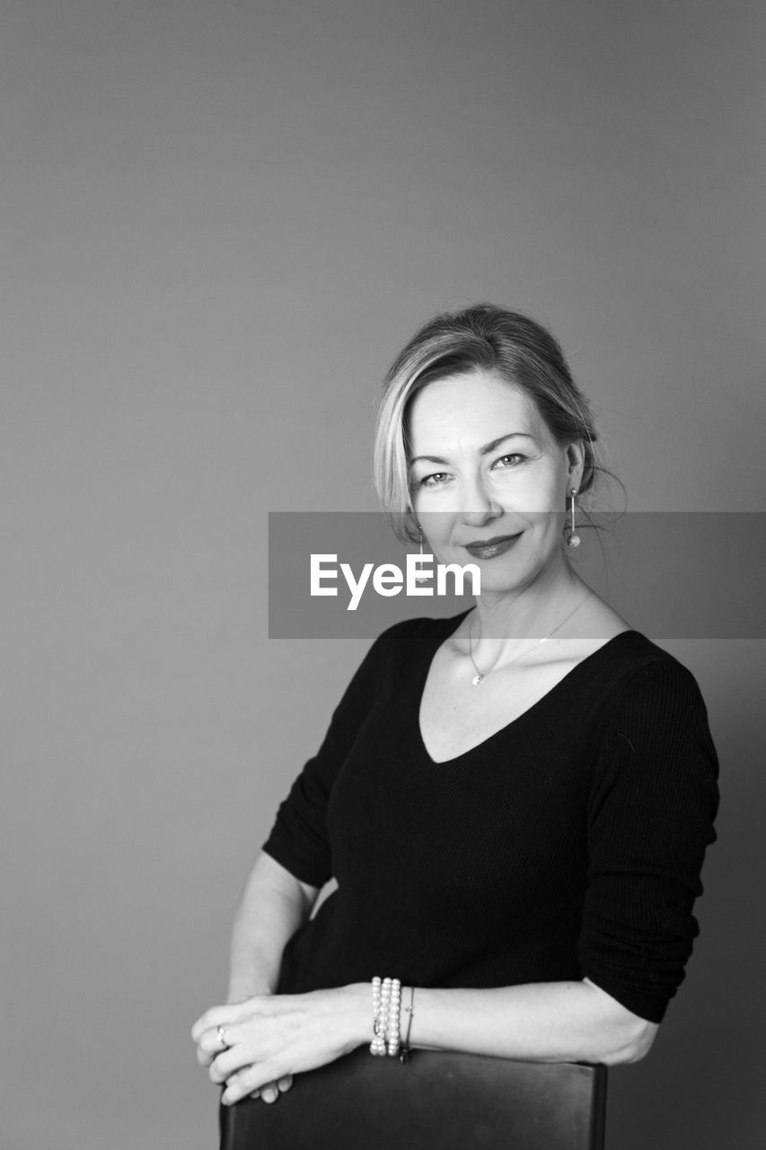 Portrait of smiling woman standing against gray background