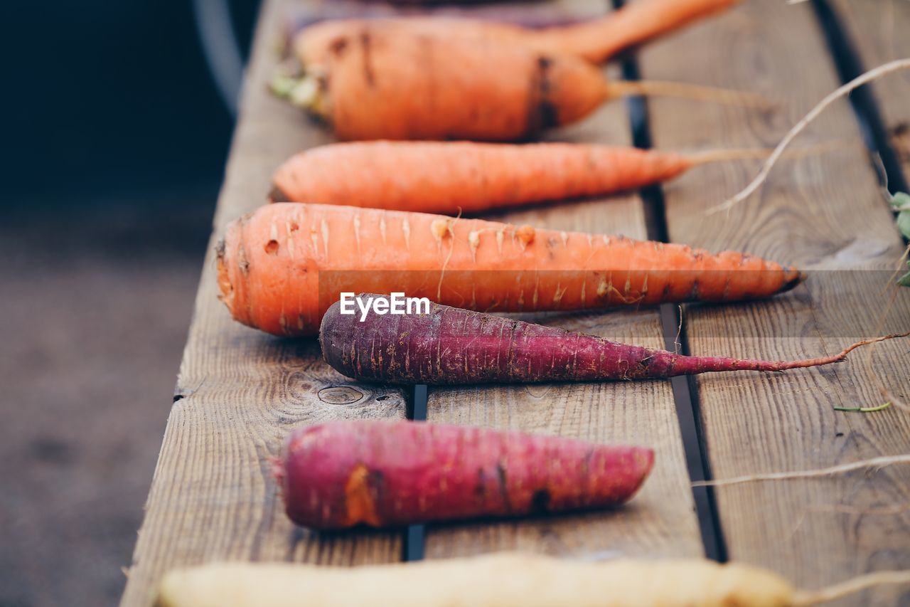 High angle view of purple and orange carrots laying on a wooden table outdoors 