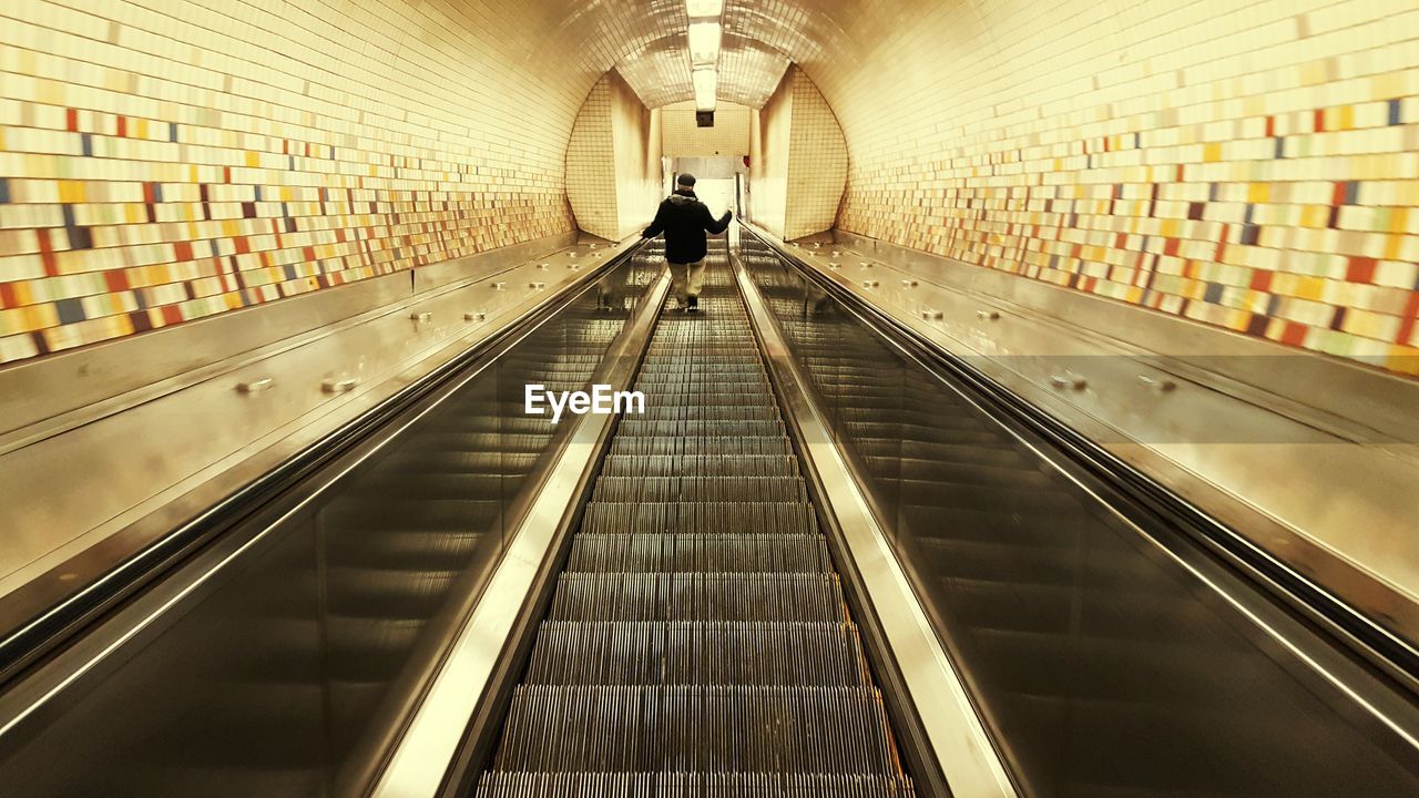 Rear view of man traveling on illuminated escalator