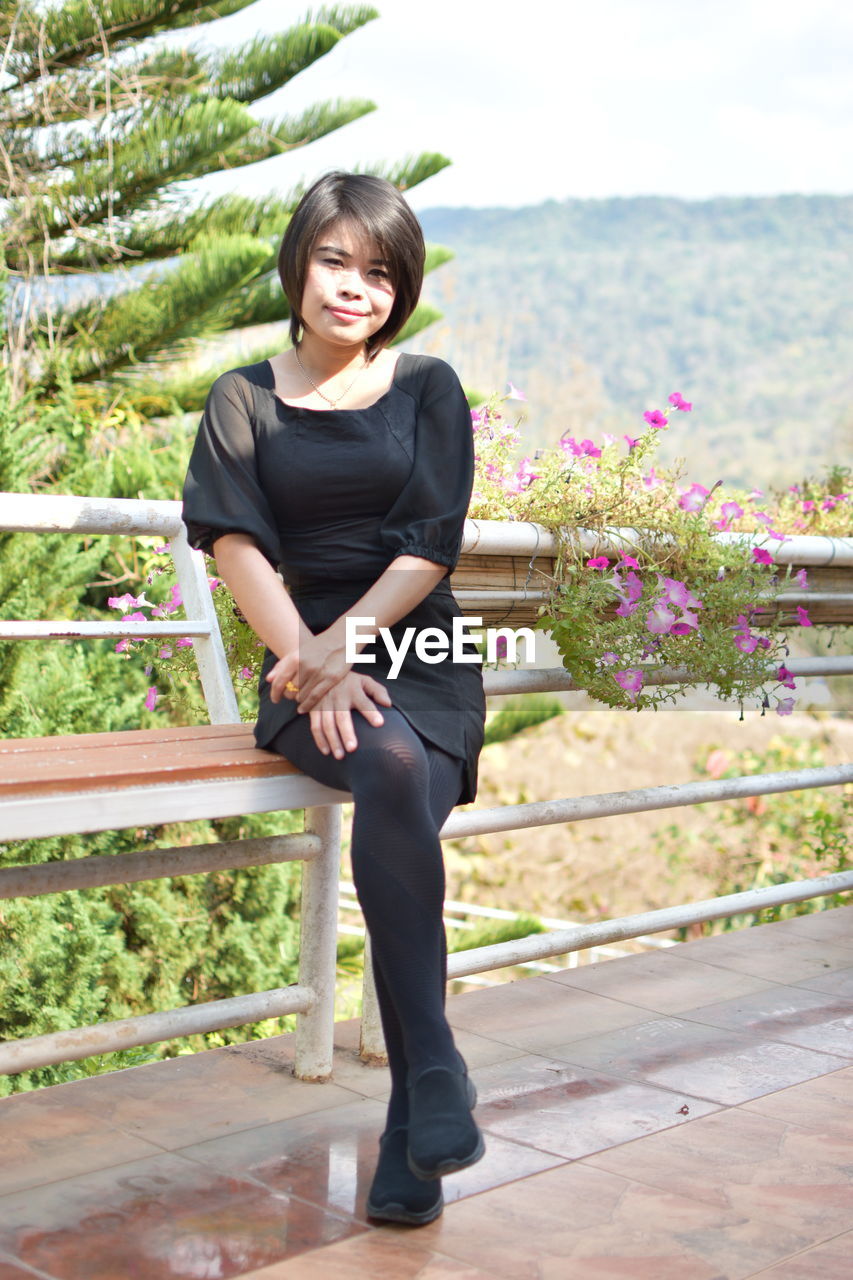 Portrait of smiling young woman sitting against railing