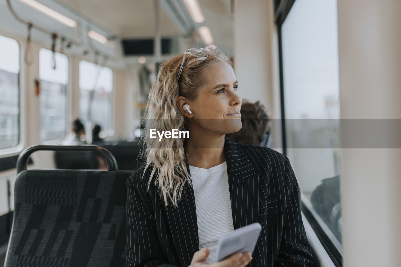 Blond businesswoman listening to music while sitting with smart phone in train