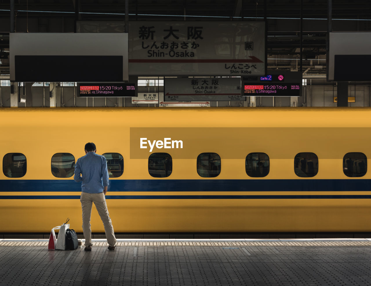 FULL LENGTH REAR VIEW OF MAN STANDING ON ILLUMINATED RAILROAD STATION PLATFORM