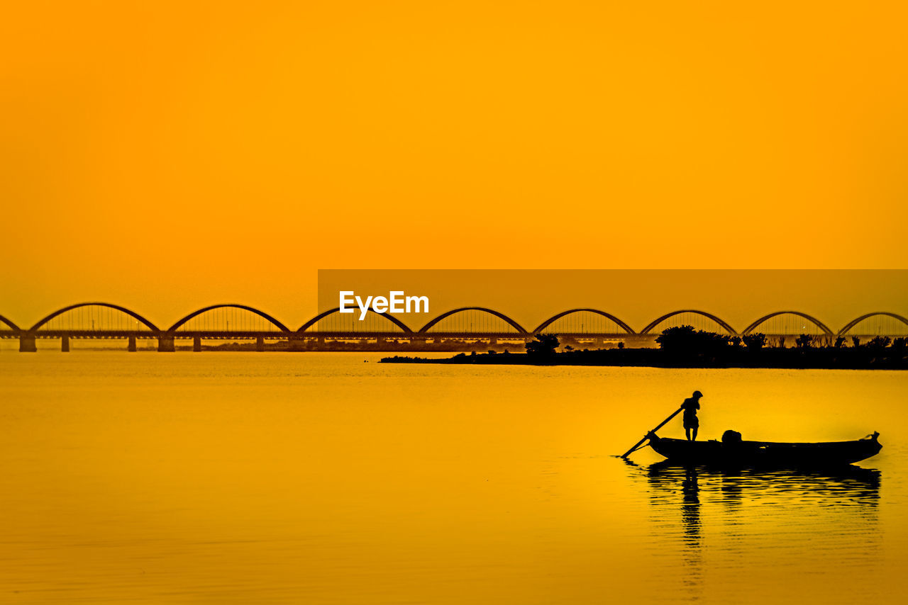 Silhouette person on boat against sky during sunset