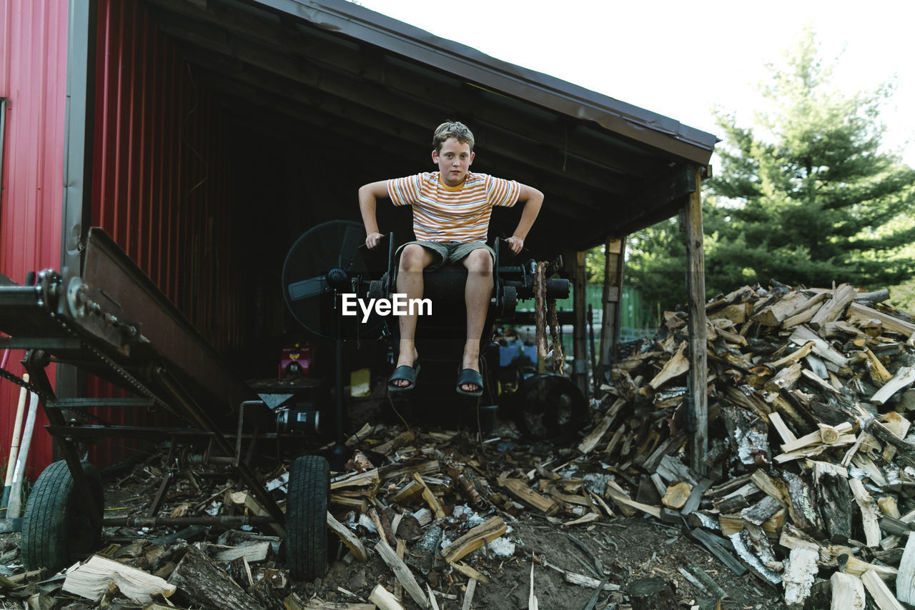 Full length of boy sitting on equipment in warehouse