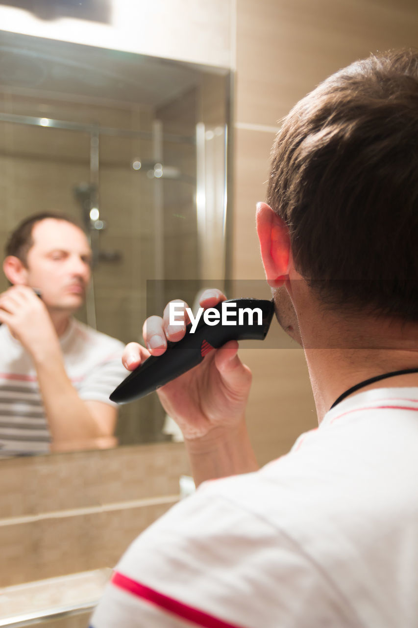 Young man trimming beard in bathroom