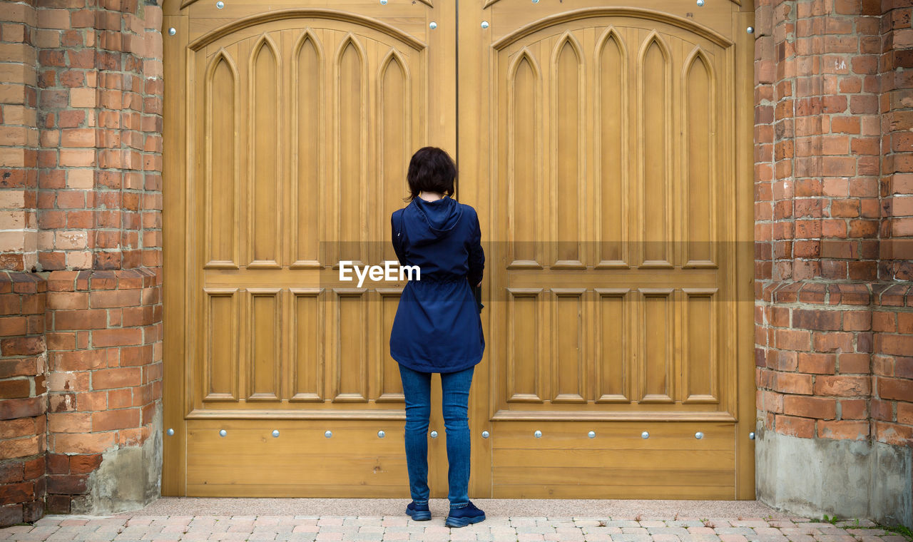 A woman is facing the huge gate of a catholic church trying to open the door.