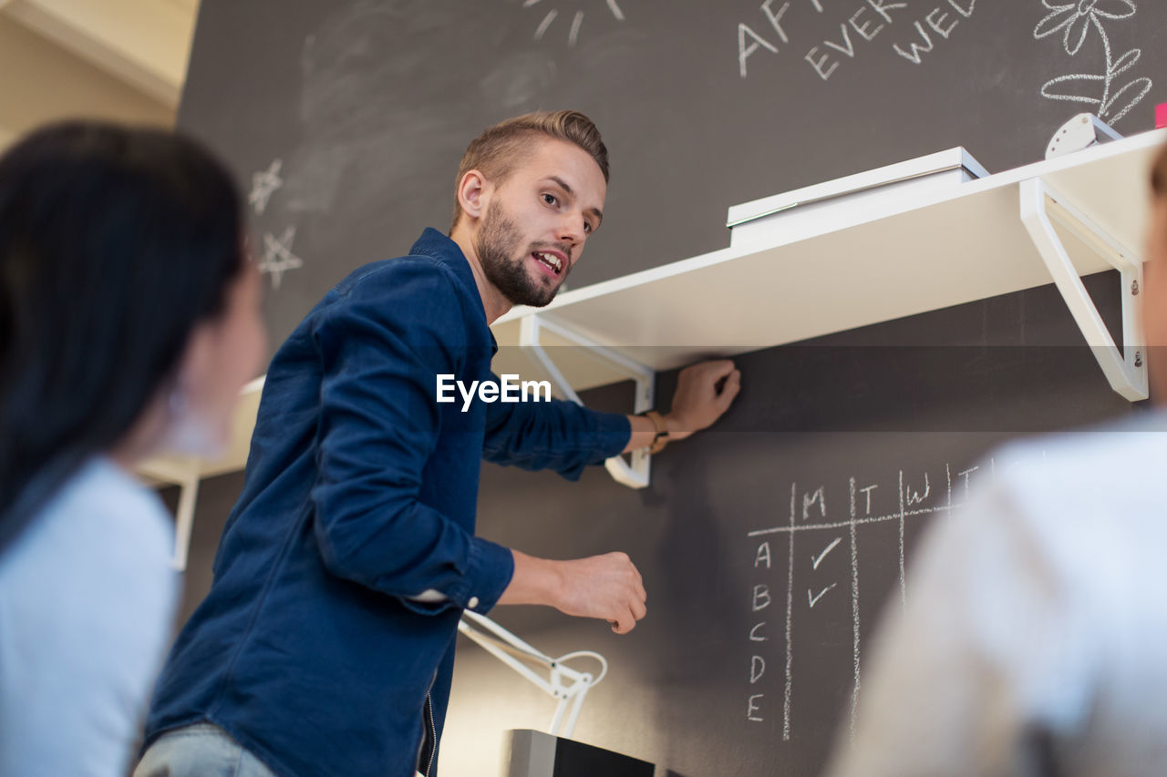 Low angle view of confident young businessman planning with female colleagues by wall at creative office