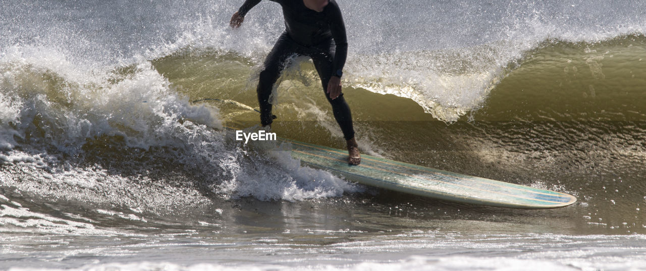 Man wearing a wetsuit surfing using a long surfboard at gilgo beach on long island.