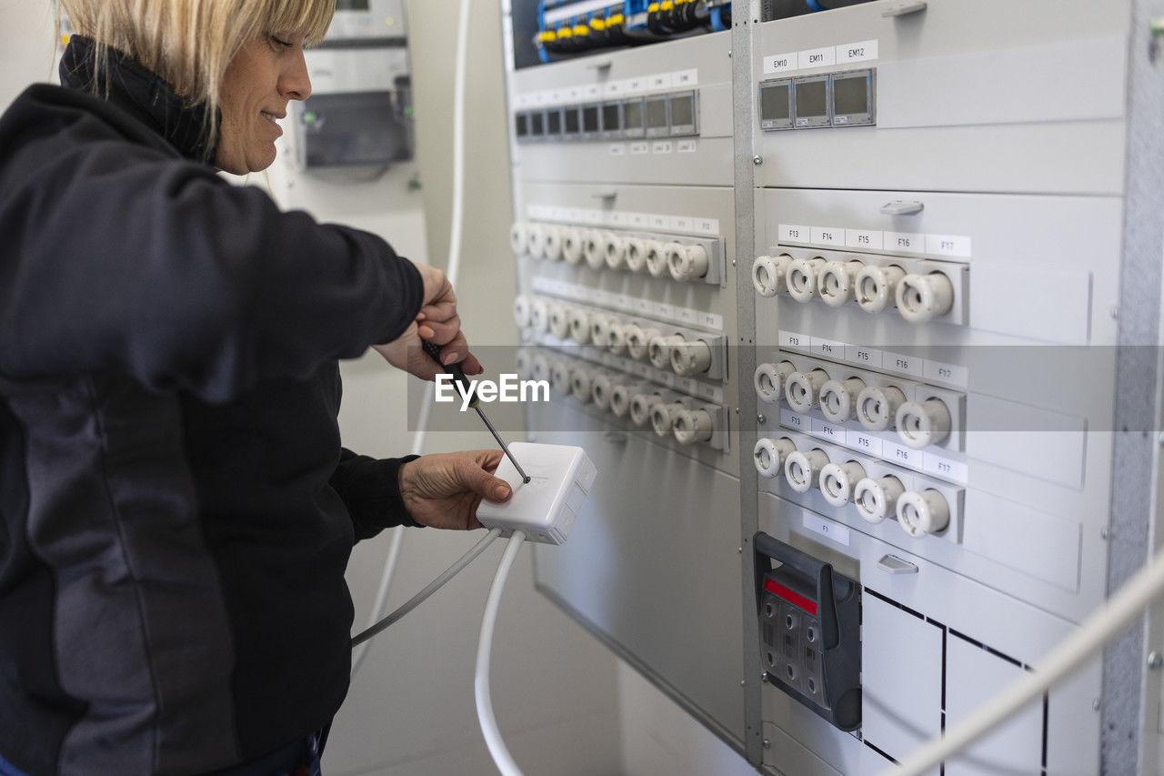 Repair woman repairing fuse box while working in meter room of industry