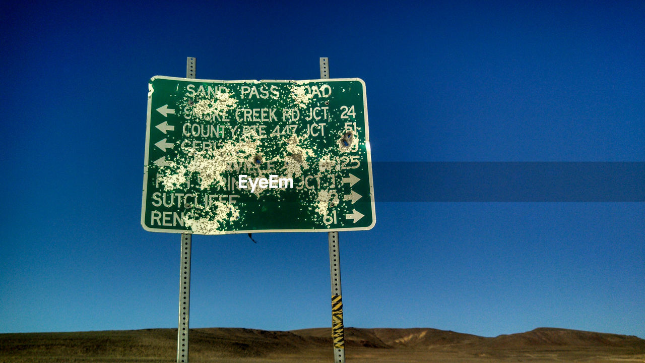 Low angle view of weathered road sign against clear blue sky