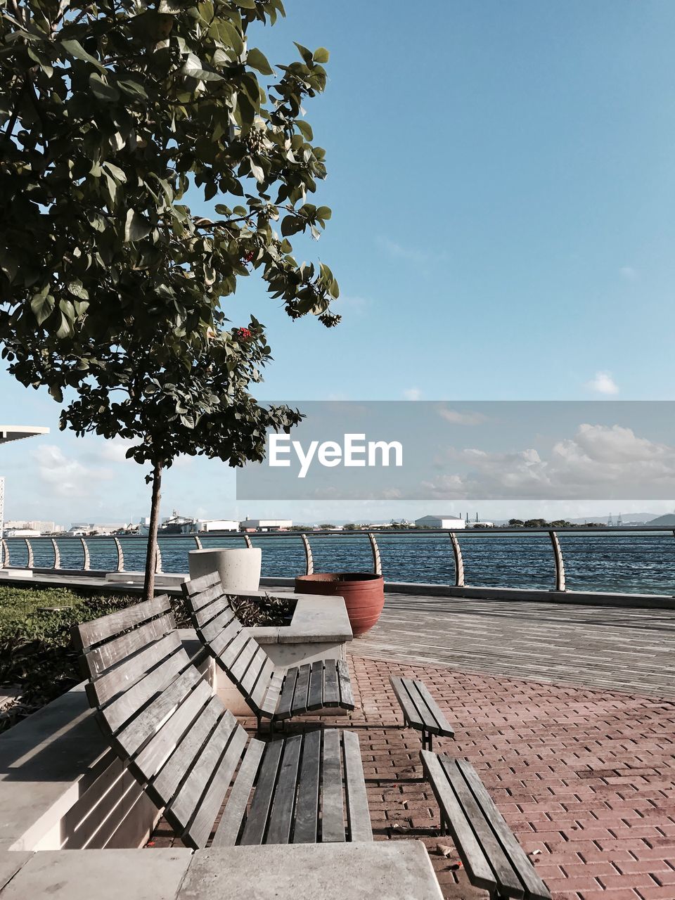 Empty park bench by sea against sky