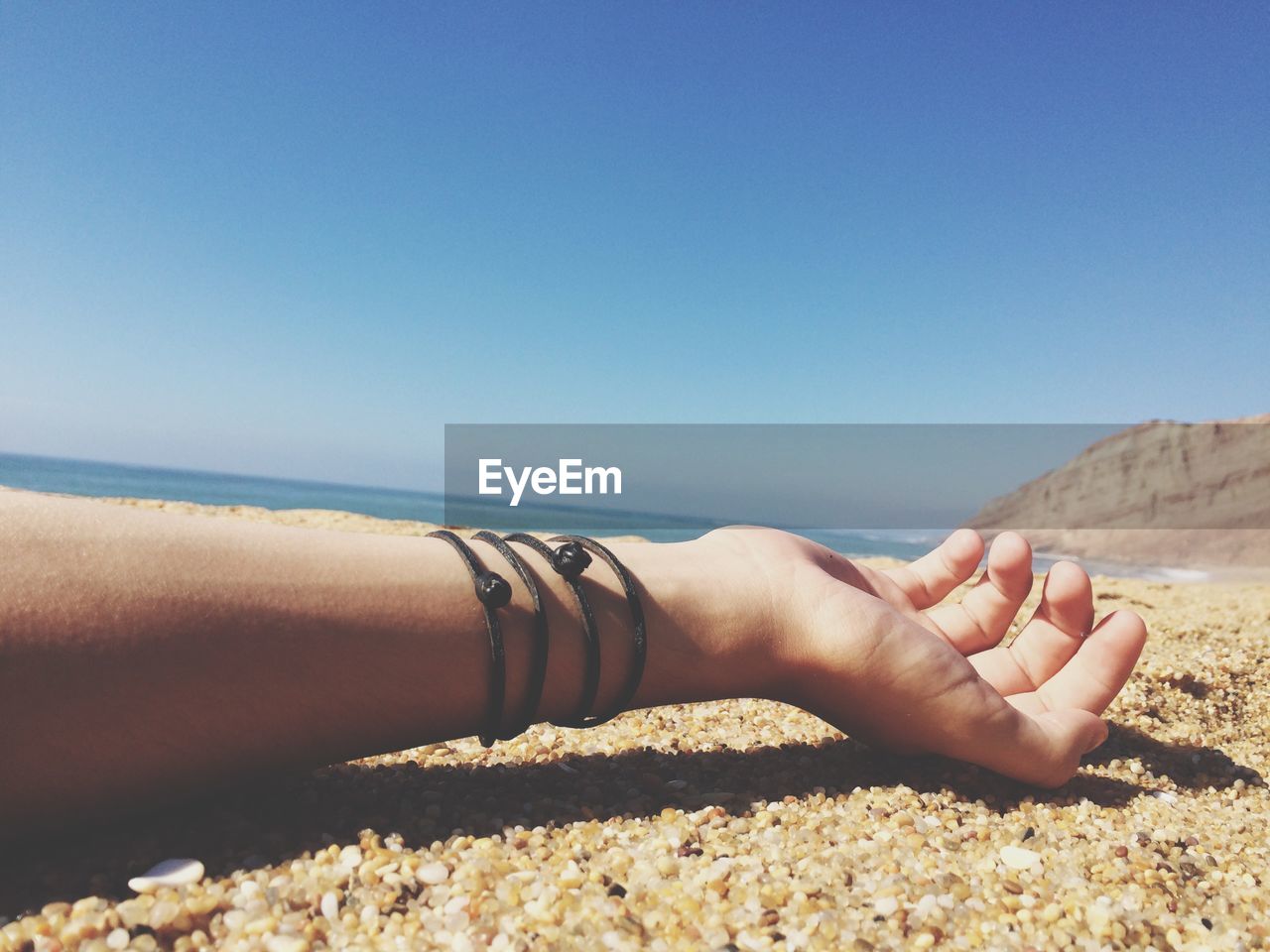 Cropped image of hand on beach against sky