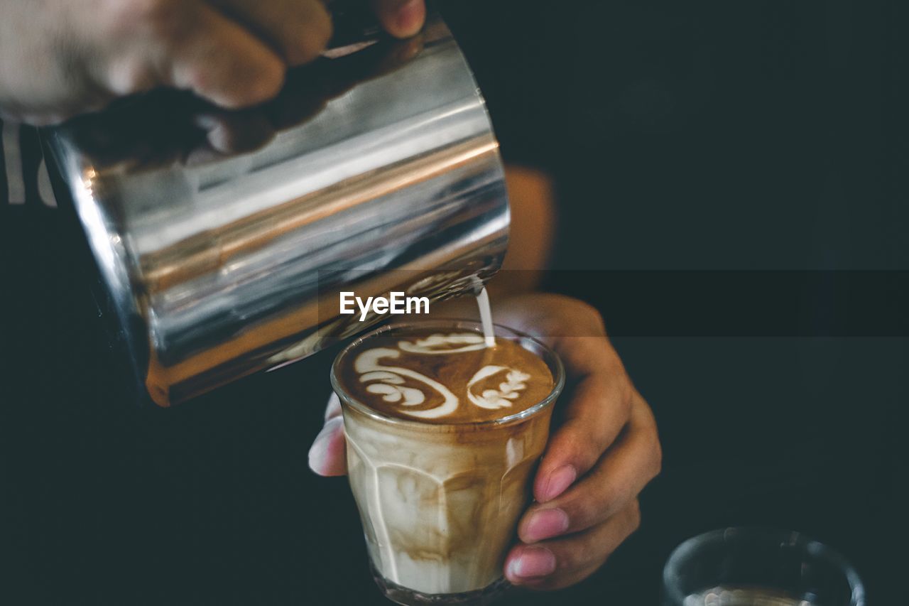 Cropped hand pouring milk in coffee over table