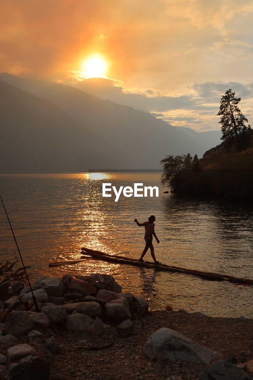 Teenager boy standing at lakeshore during sunset