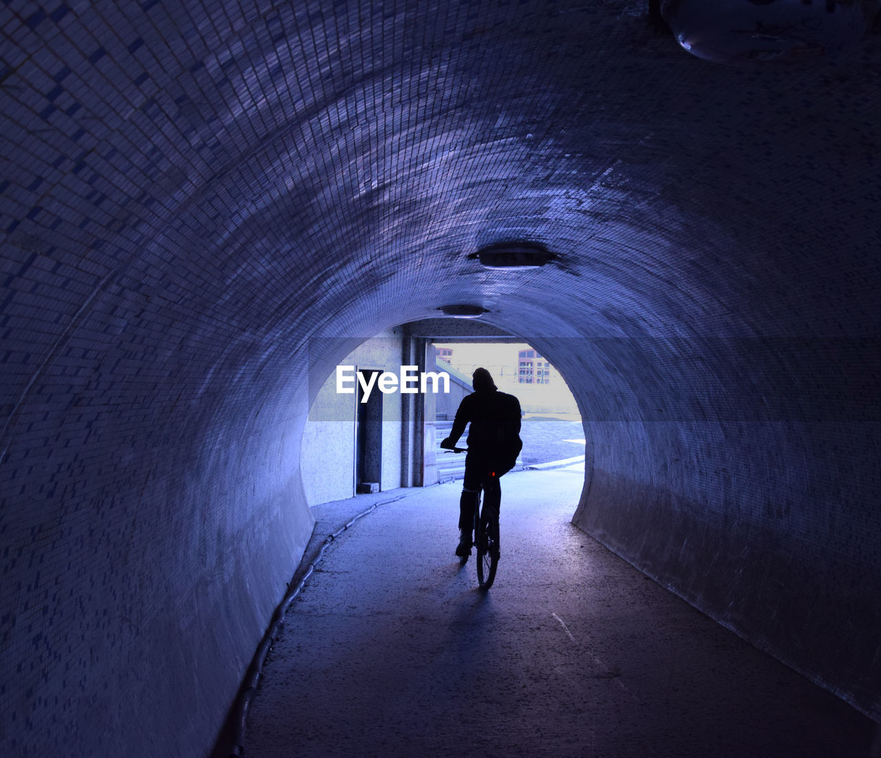 Rear view of person riding bicycle through tunnel