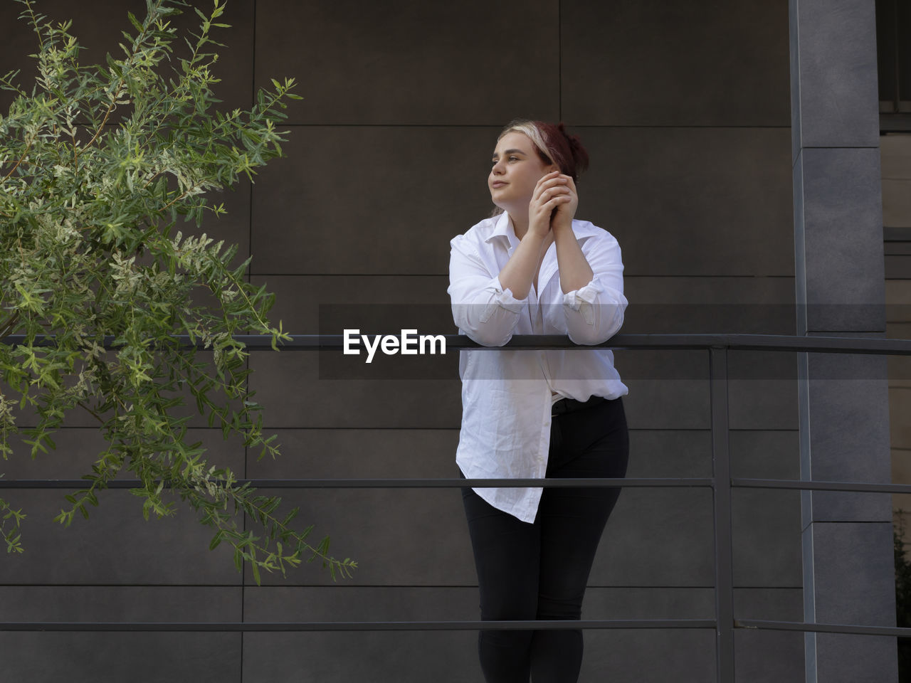 Bottom view high-rise building with tree, young business woman 20s looking around. caucasian