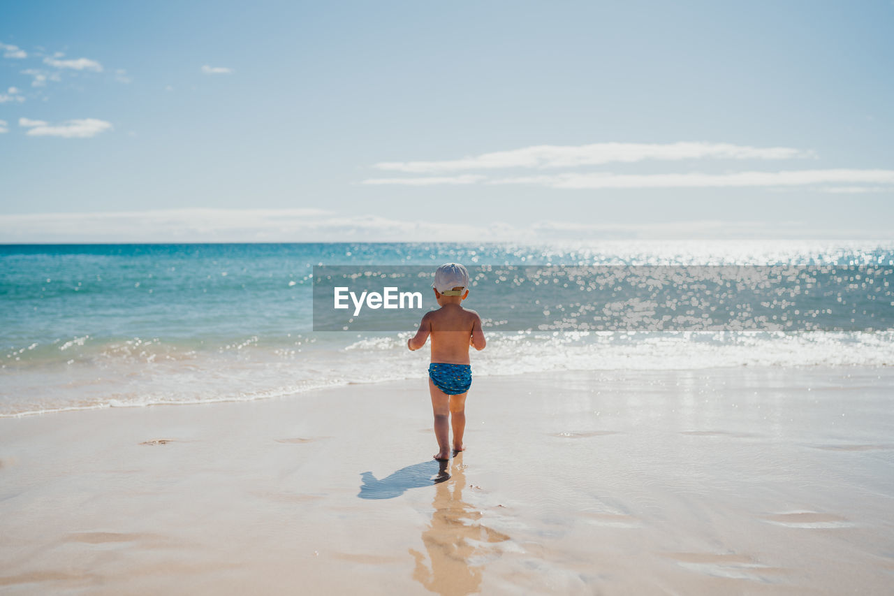 Boy walking into the water at the beach on a sunny day on vacation