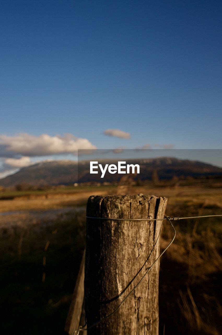 Close-up of wooden post on field against sky