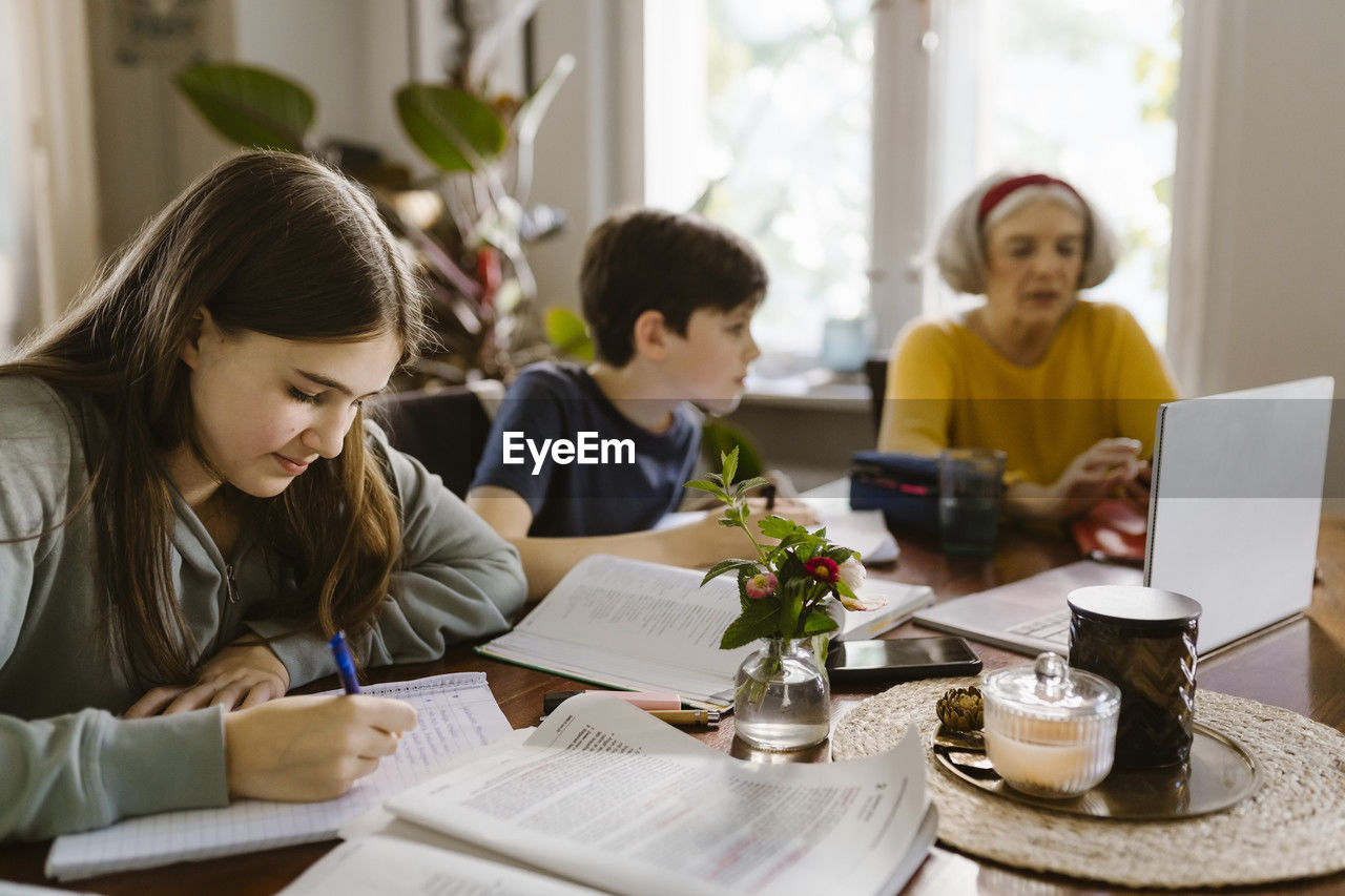 Girl doing homework while sitting with brother and grandmother at home