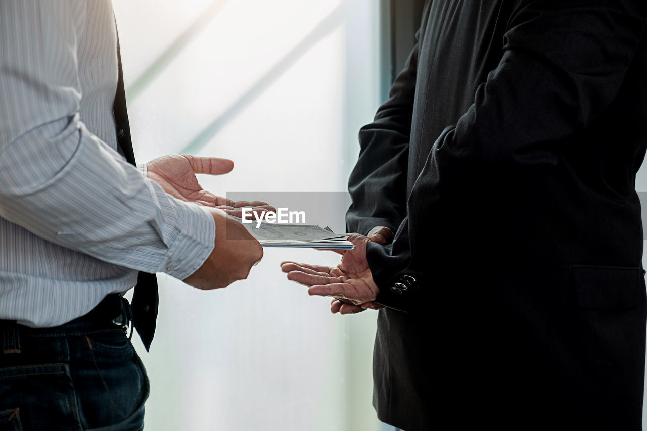 Midsection of man bribing businessman in office