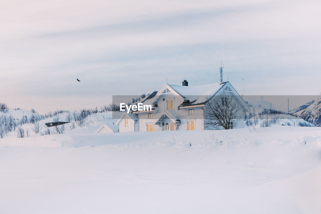 House on snow covered field by building against sky