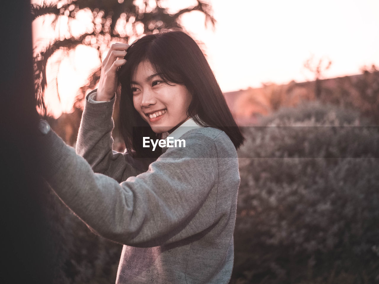 Smiling young woman standing against plants