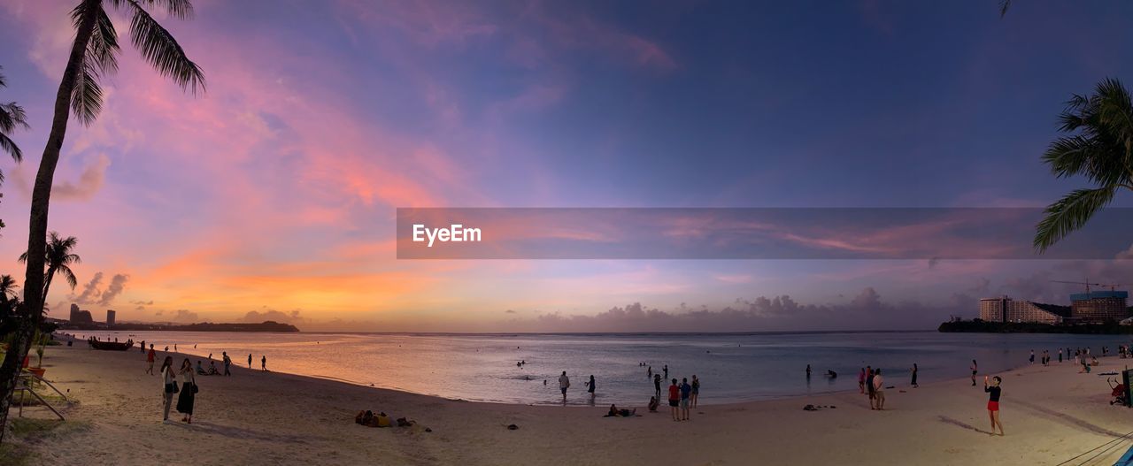 People at beach against sky during sunset