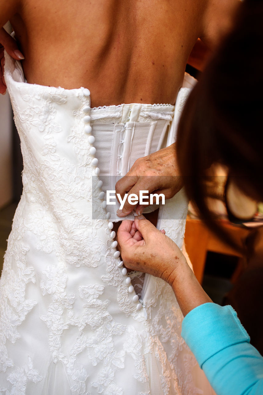 Close-up of a mother button up the white wedding dress of her daughter