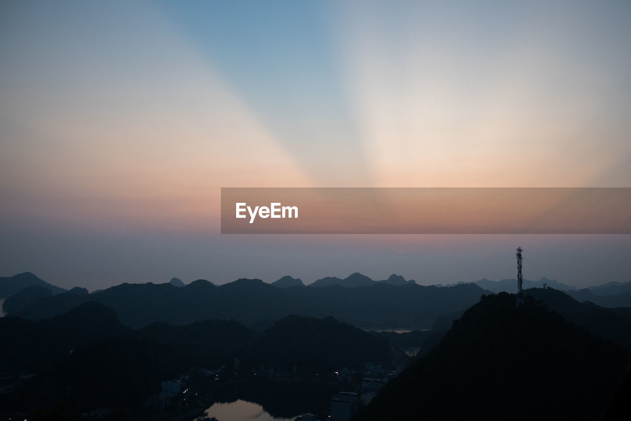 SILHOUETTE BUILDINGS AND MOUNTAINS AGAINST SKY DURING SUNSET