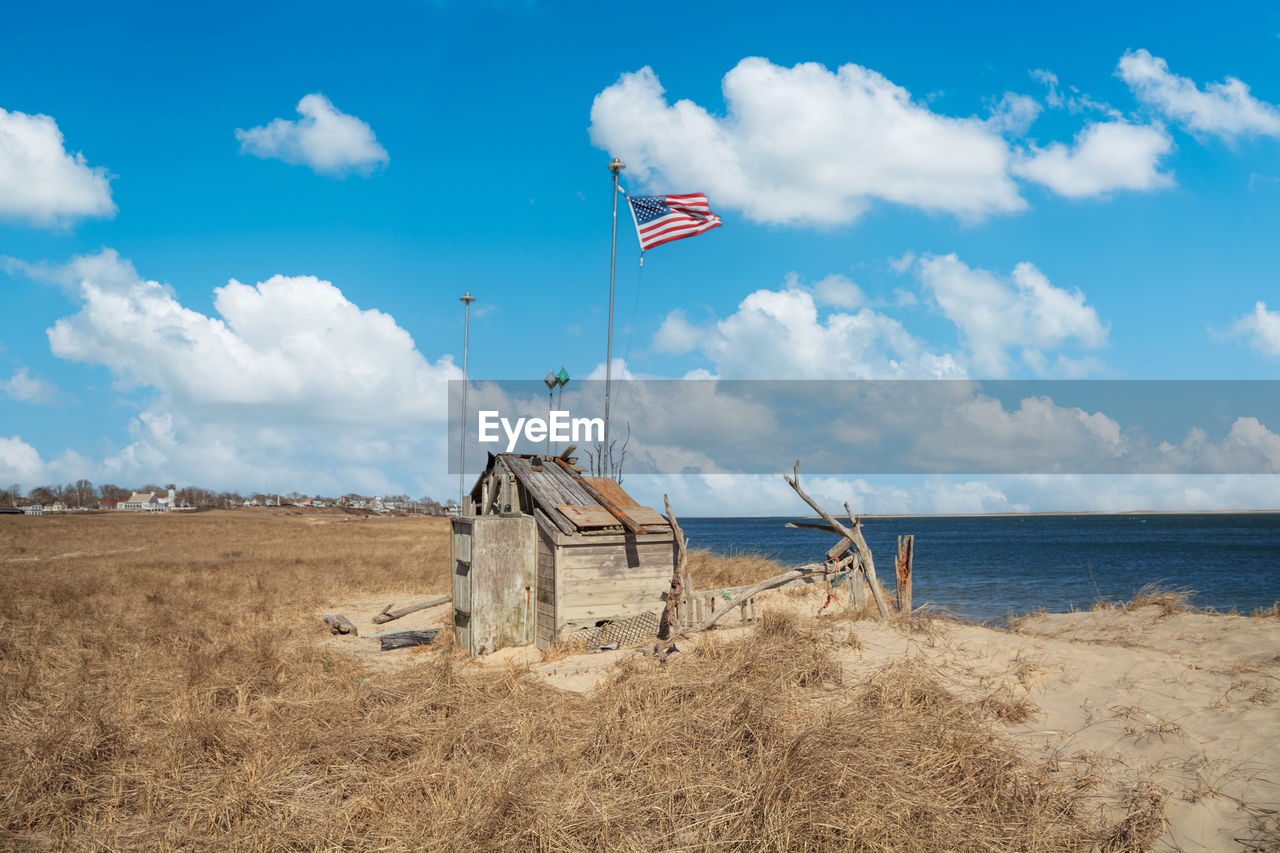 sky, land, flag, sea, cloud, nature, beach, sand, environment, wind, natural environment, water, coast, patriotism, blue, day, scenics - nature, landscape, horizon, no people, shore, outdoors, travel destinations, ocean, hut, architecture, tranquility, tranquil scene, travel, beauty in nature, sunlight, built structure, horizon over water