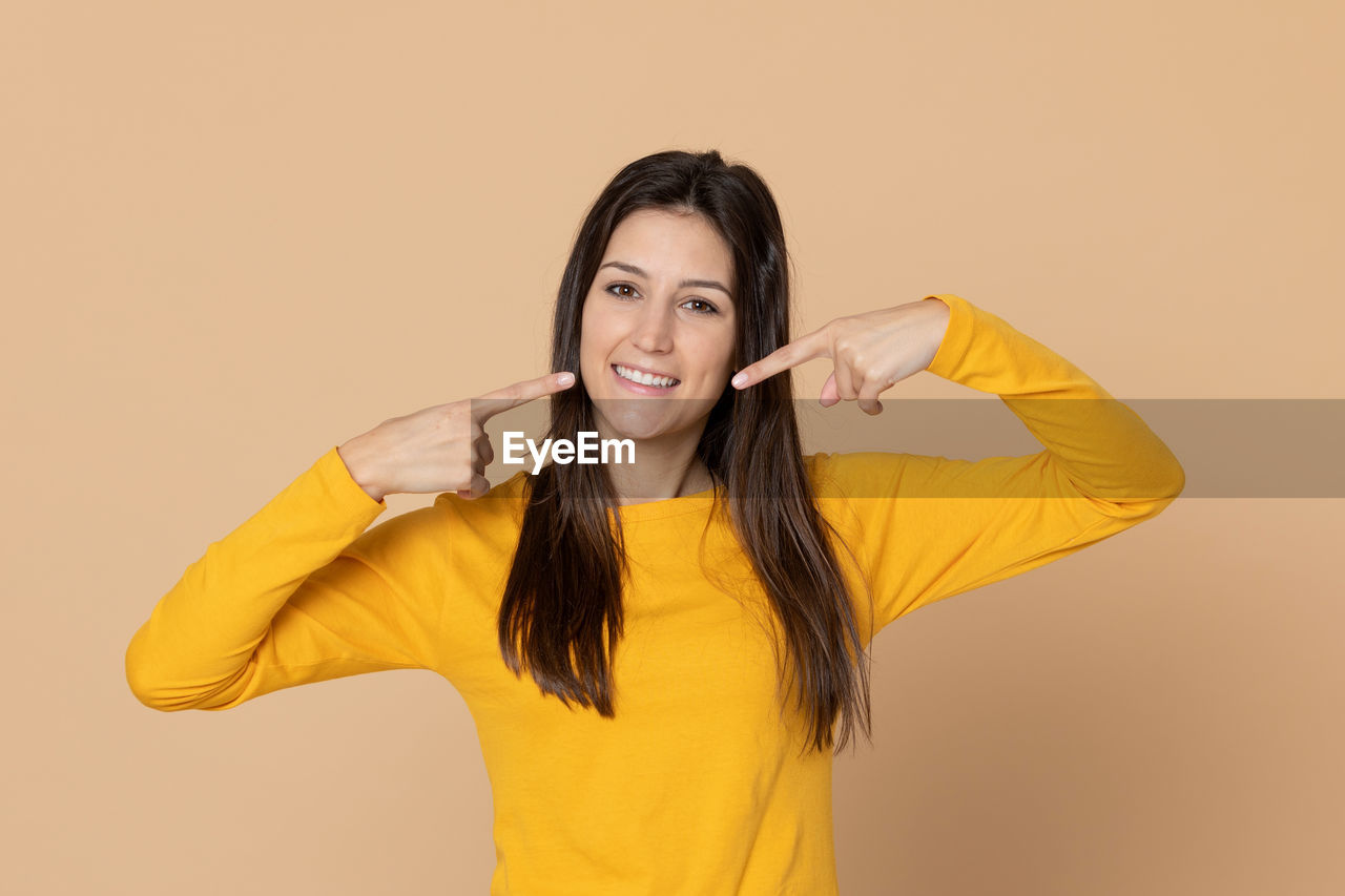 PORTRAIT OF A SMILING YOUNG WOMAN OVER YELLOW BACKGROUND