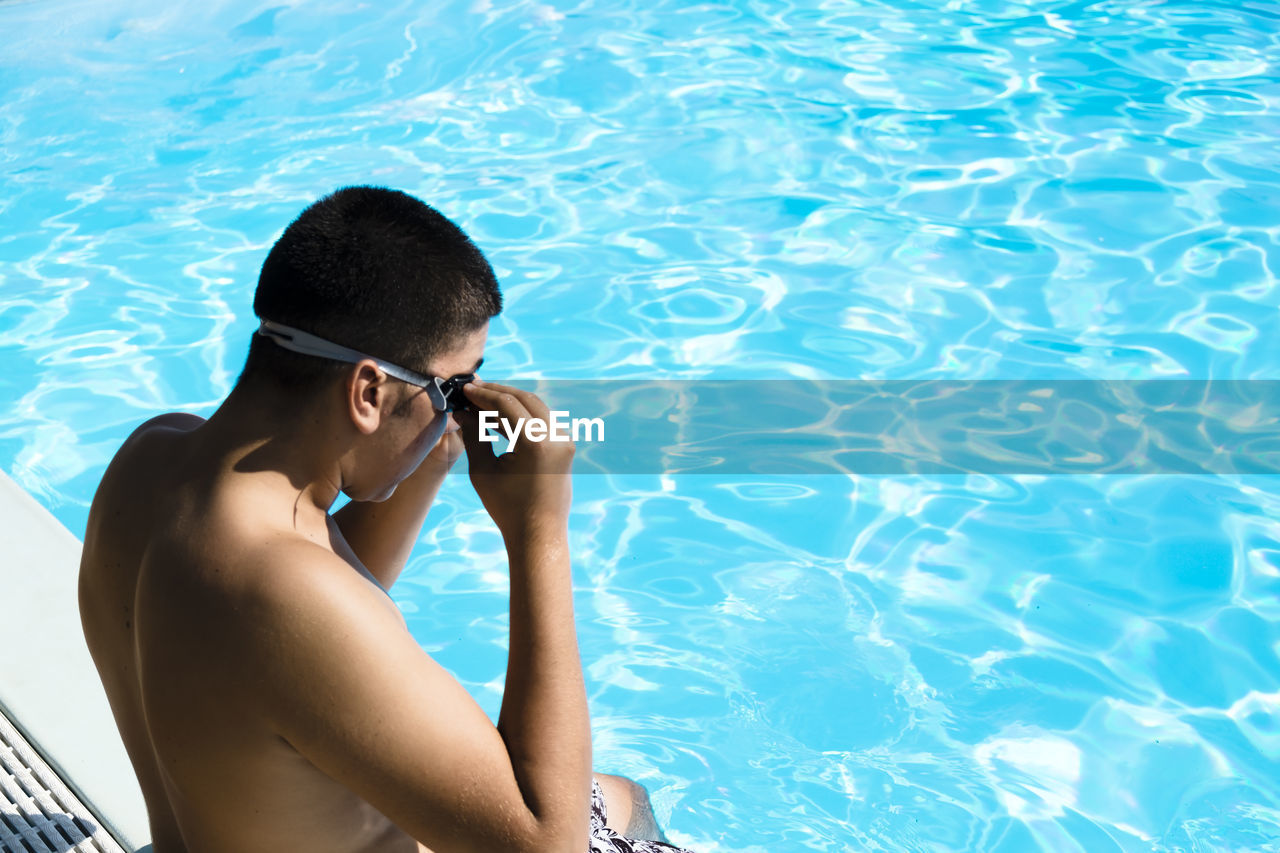 High angle view of shirtless man wearing goggles while sitting by pool