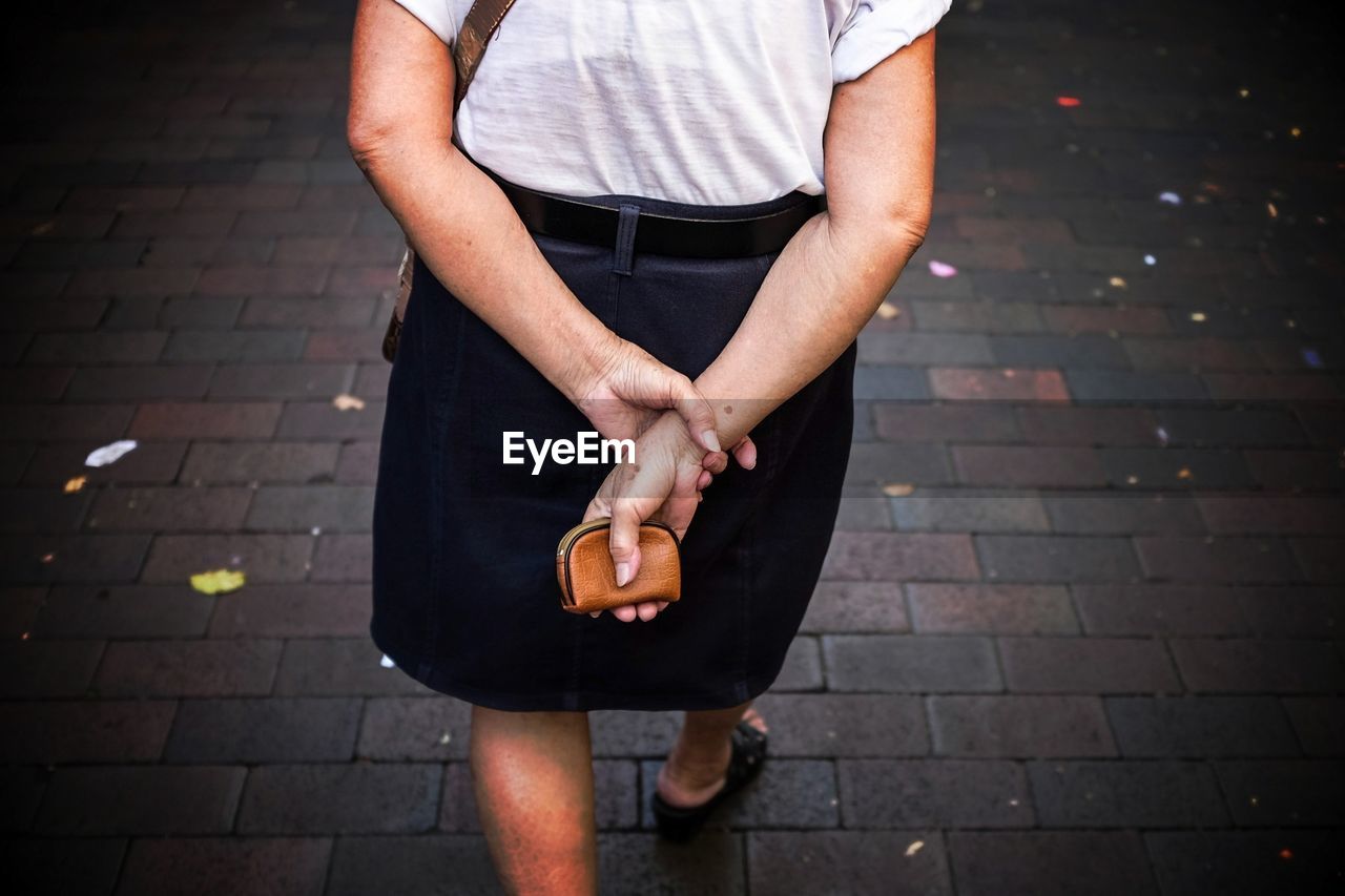 Midsection of woman holding purse and walking on street