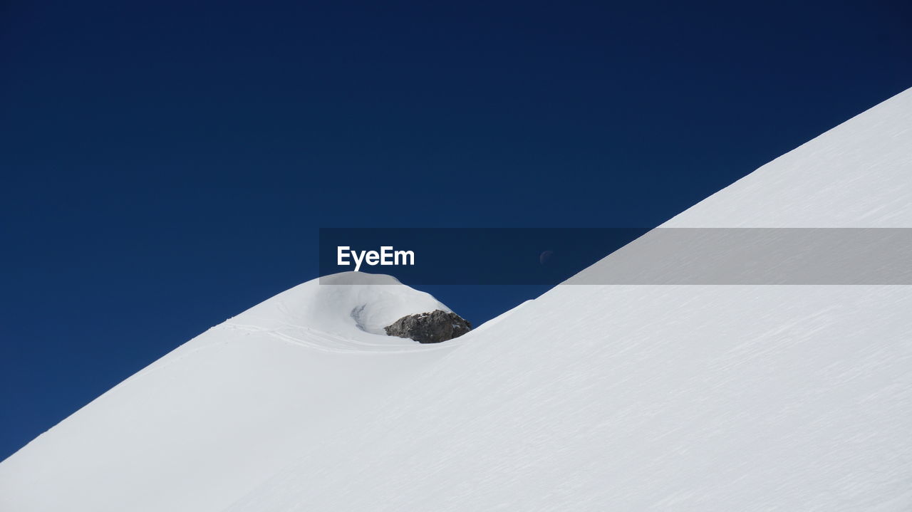 Low angle view of snow mountain against clear blue sky