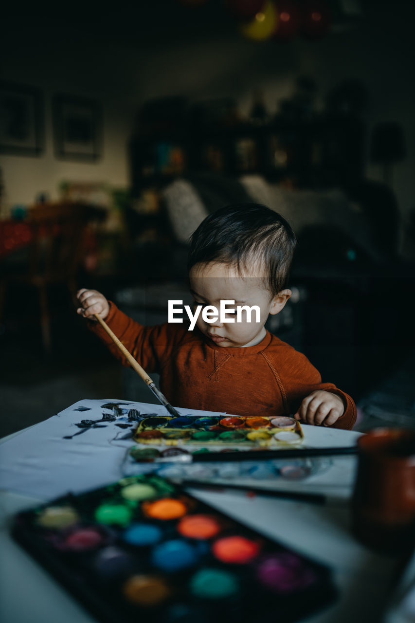 Baby boy with art and craft equipment on table at home