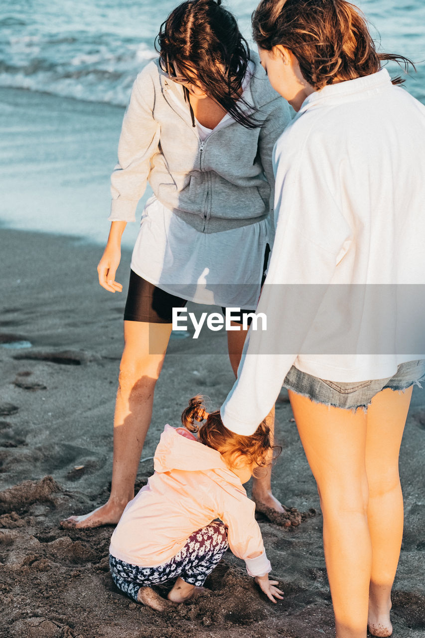 Women looking at girl playing with sand on beach