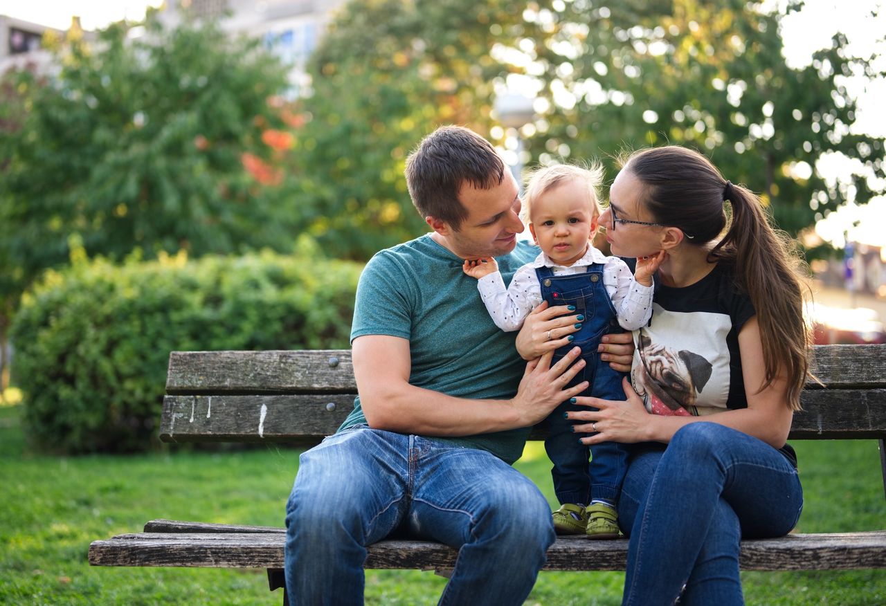 Couple sitting on a bench in a park holding their little child