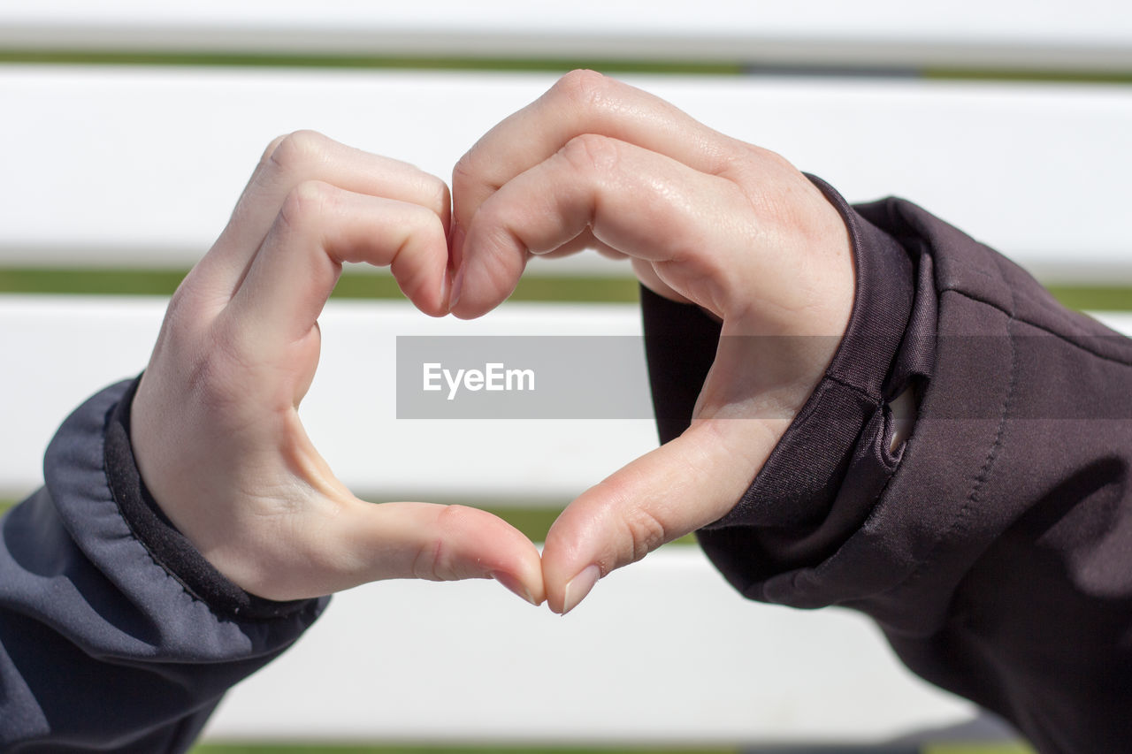 Cropped image of couple forming heart shape against wall